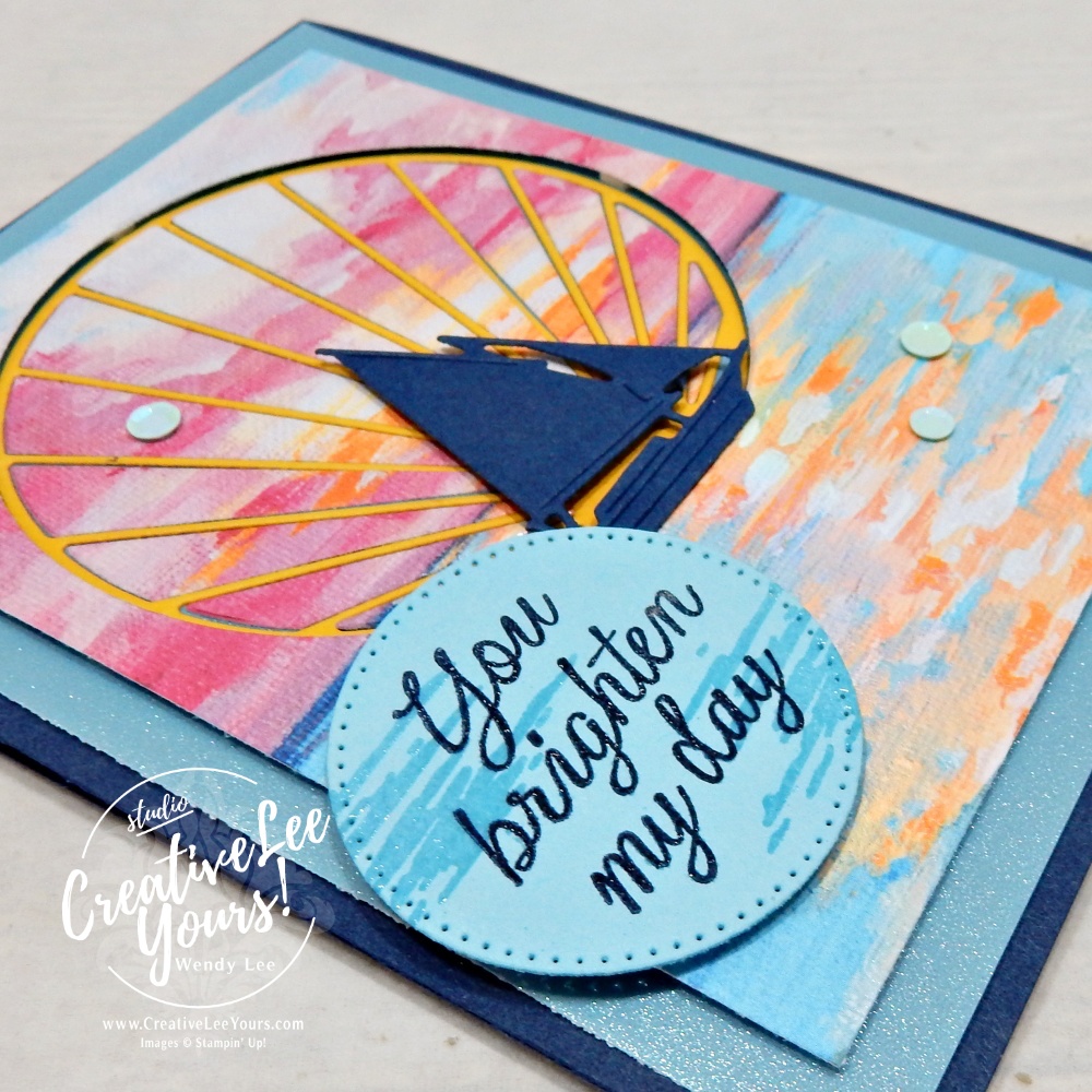 Close-up of inlaid sun ray die cut and sailboat embellishment layered over Scenic Coast sunset designer paper.