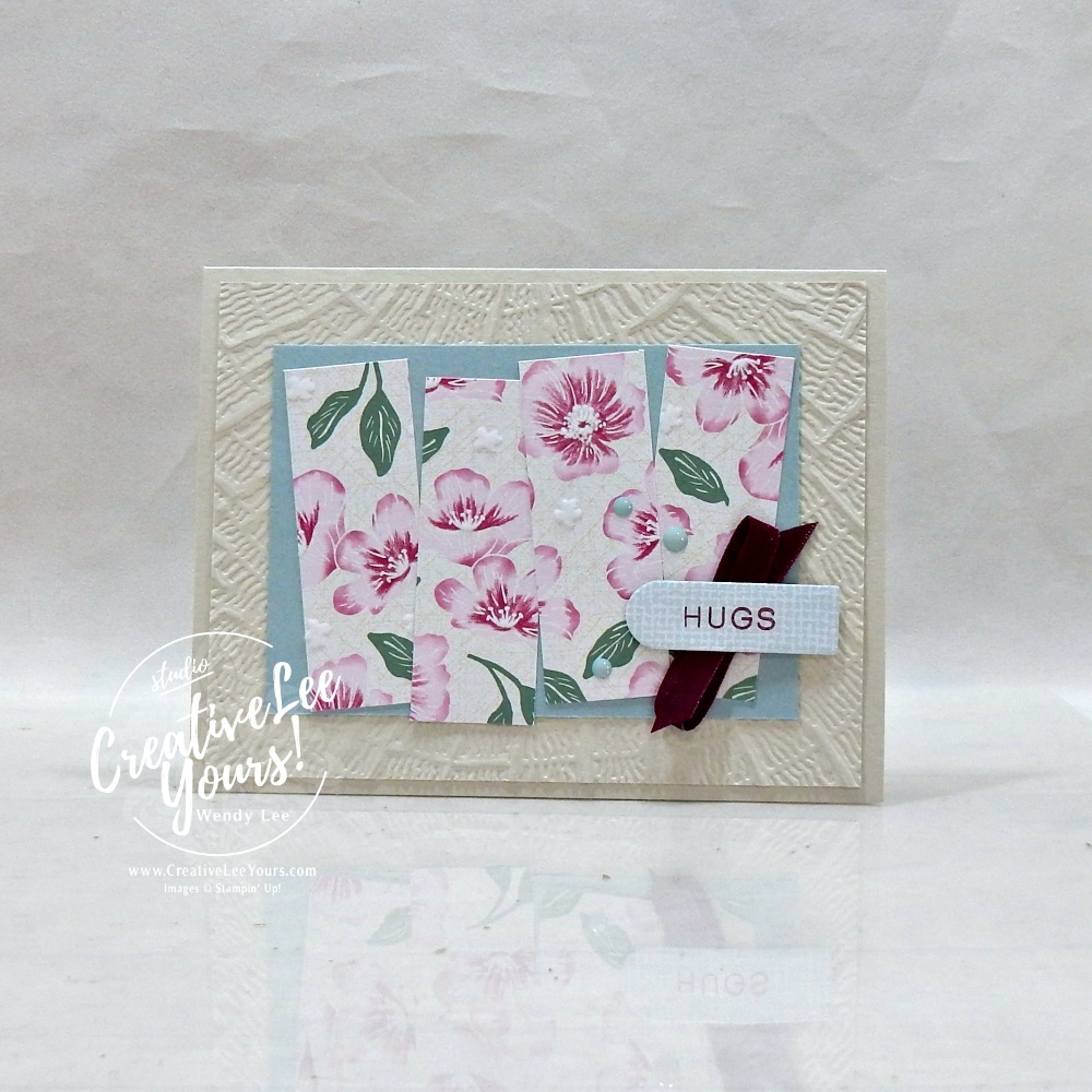 Handmade floral greeting card featuring textured embossed background, designer paper strips, satin ribbon, scalloped sentiment label, and layered embellishments.
