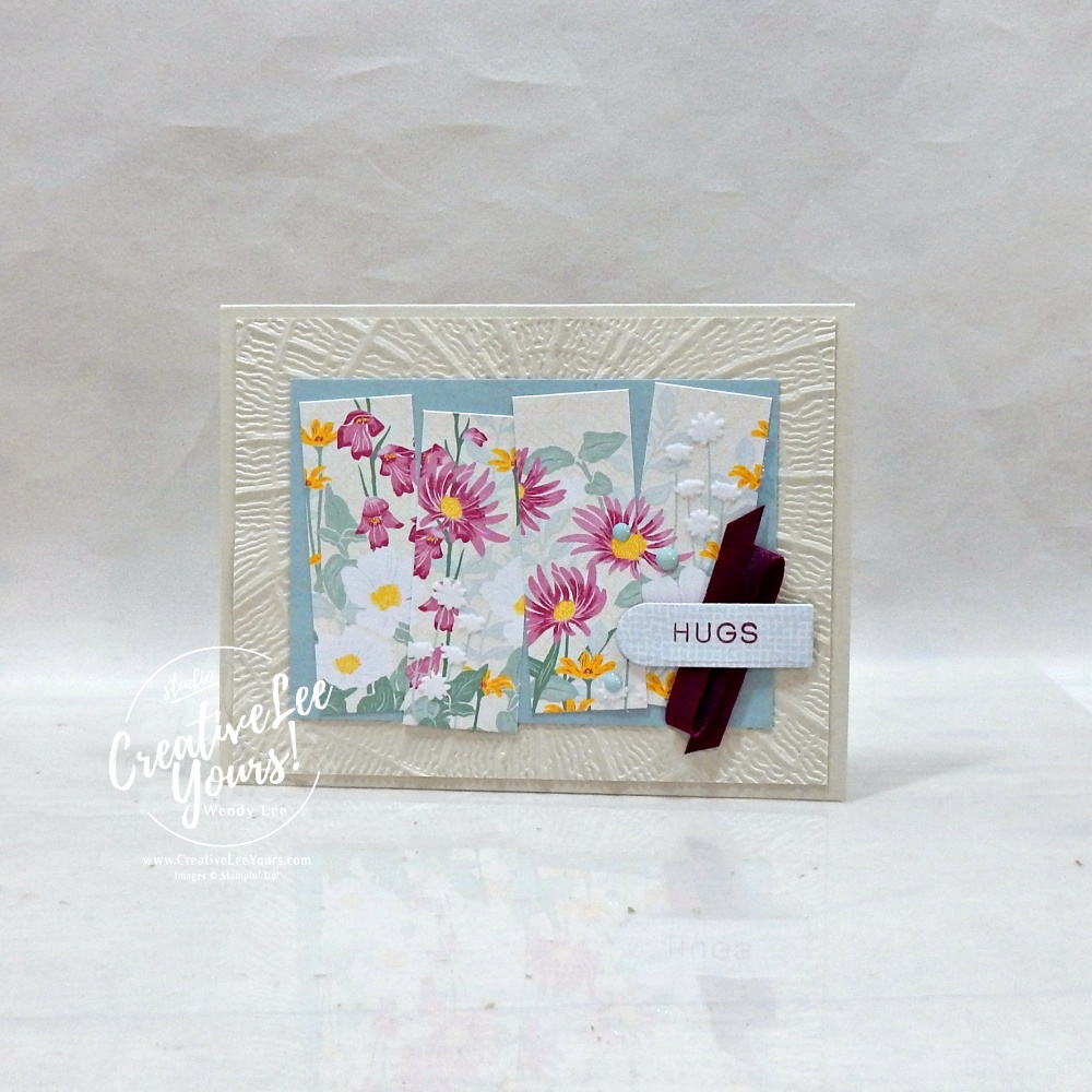 Handmade floral greeting card featuring textured embossed background, designer paper strips, satin ribbon, scalloped sentiment label, and layered embellishments.