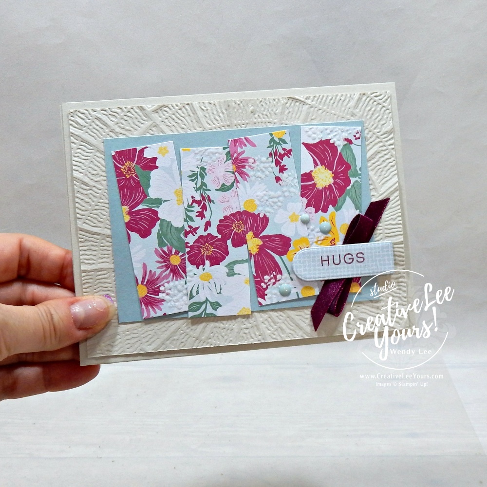 Handmade floral greeting card featuring textured embossed background, designer paper strips, satin ribbon, scalloped sentiment label, and layered embellishments.