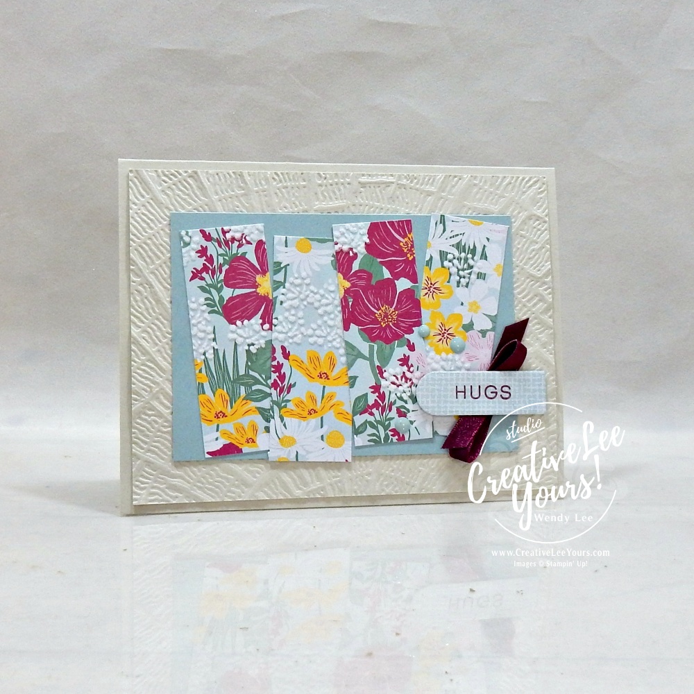 Handmade floral greeting card featuring textured embossed background, designer paper strips, satin ribbon, scalloped sentiment label, and layered embellishments.